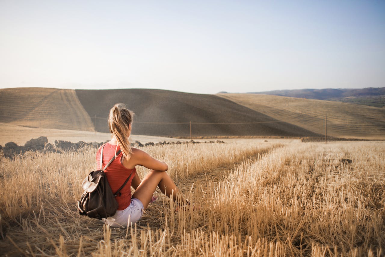 team-06 Woman sitting with backpack in rural wheat field, enjoying serene summer landscape.