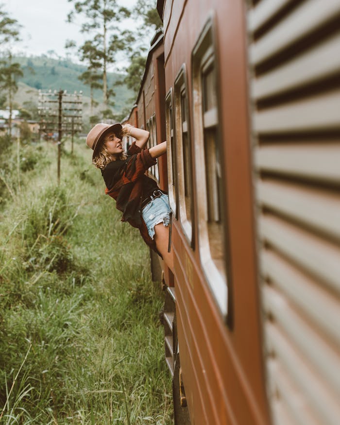team-01 A joyful young woman embraces freedom as she leans out of a passenger train window traveling through lush countryside.