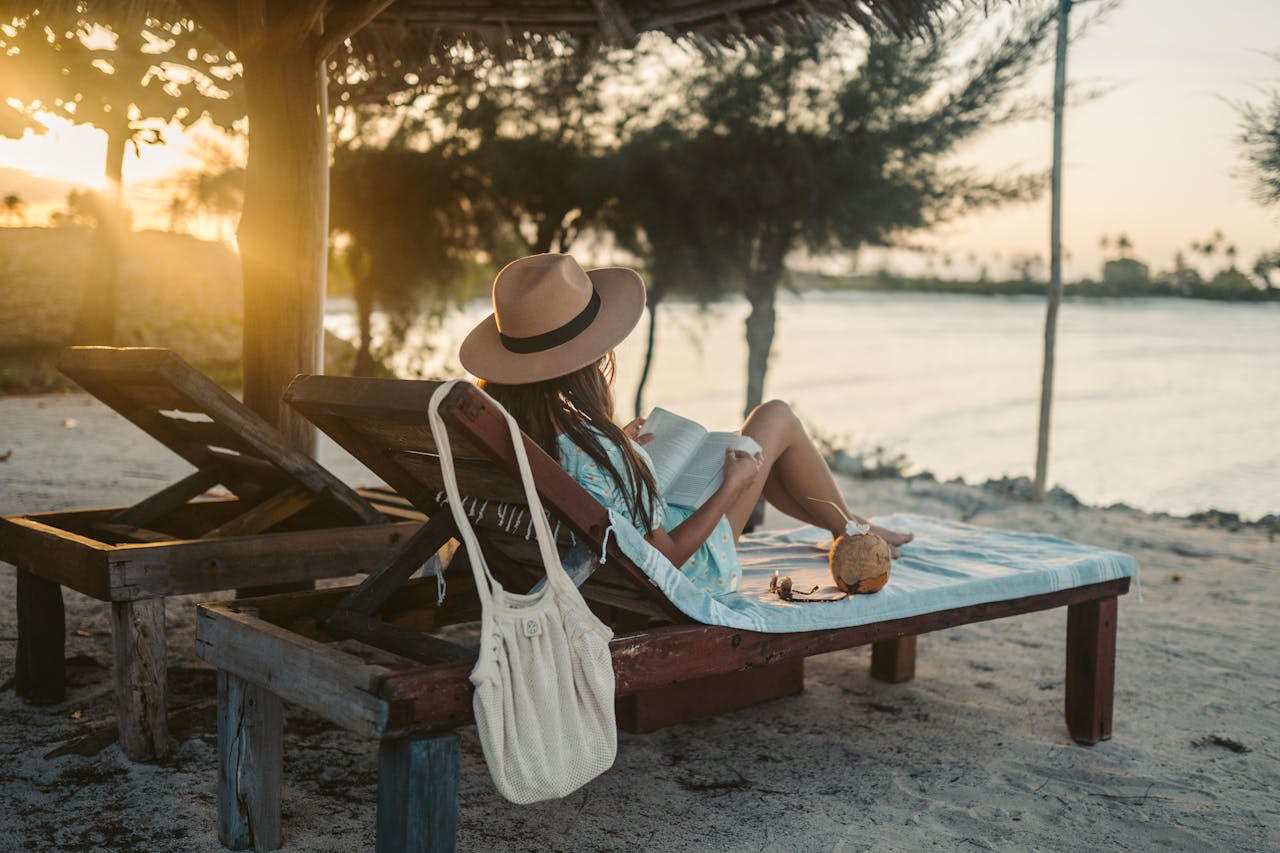 home-hero Woman reading on a beach lounger under a sun hat in Zanzibar at sunset, embracing vacation tranquility.