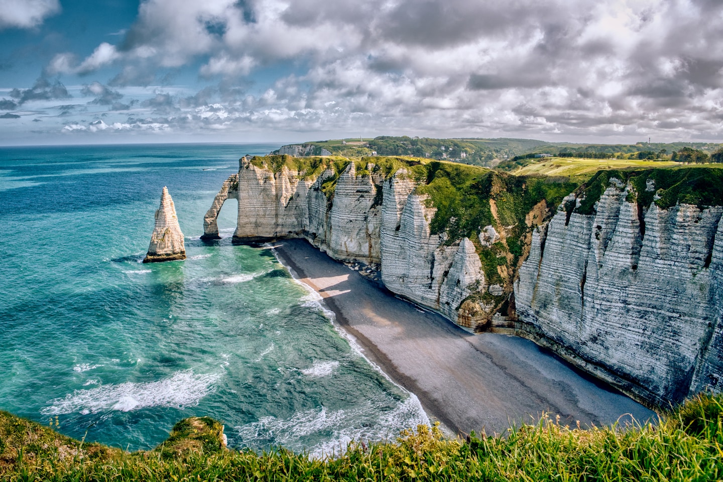 green and gray rock formation beside body of water under cloudy sky during daytime